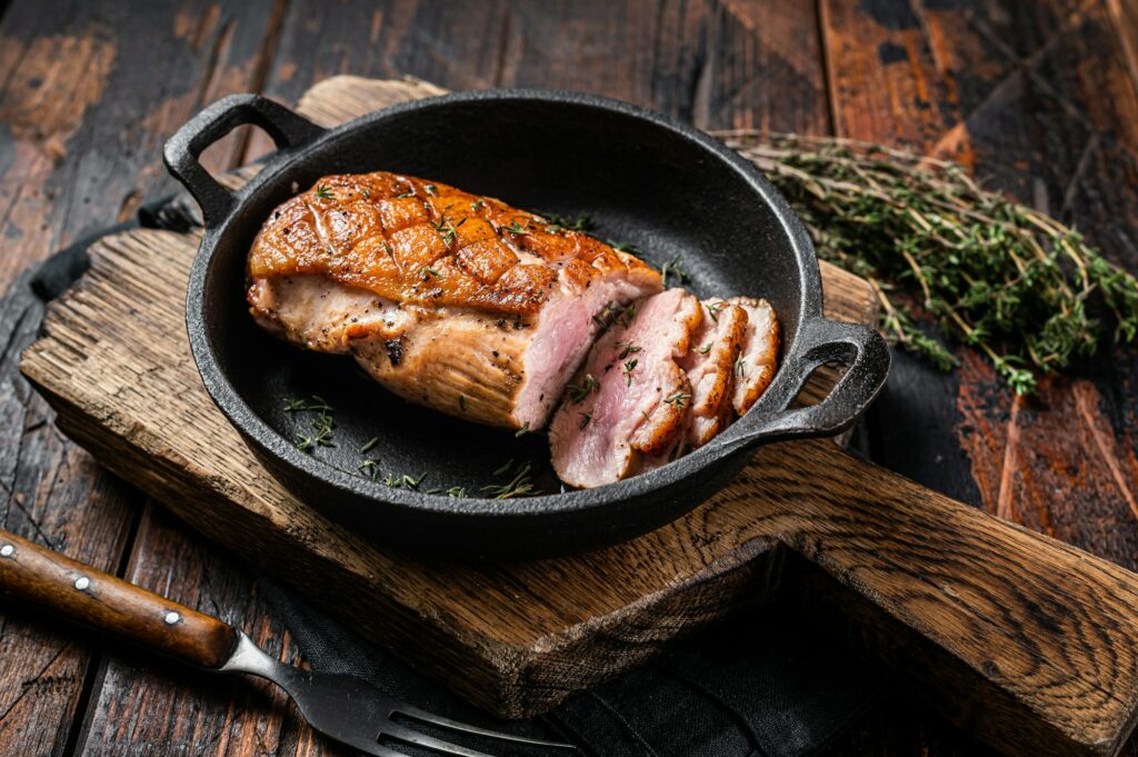 Duck breast roasted in a pan, poultry meat steak with herbs. Wooden background. Top view