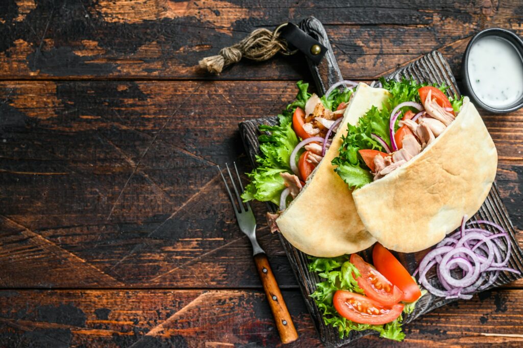 Greek gyros wrapped in pita breads with vegetables and sauce. Dark wooden background